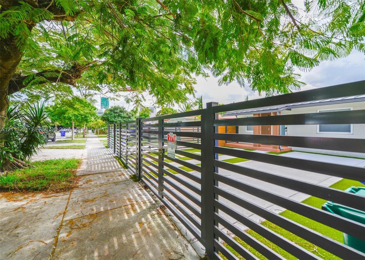 Horizontal slat metal fencing, gated entry, concrete driveway, and mature landscaping