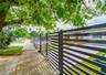 Horizontal slat metal fencing, gated entry, concrete driveway, and mature landscaping