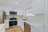 Modern kitchen featuring high-gloss white cabinetry, light-toned stone-finish countertops, stainless steel appliances, and wood-finish flooring