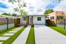 Single-story exterior featuring a metal roof, concrete driveway, synthetic turf lawn, stone paver walkway, and horizontal slat privacy fencing