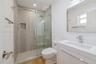 Bathroom featuring a glass-enclosed shower with floor-to-ceiling tile, built-in recessed niche, modern vanity with a white countertop, and wood-finish