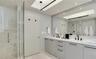 Dual-sink vanity with light-gray cabinetry, stone countertops, matte black fixtures, full-width mirror, and walk-in tiled shower with a glass enclosur