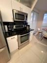 Kitchen featuring white shaker-style cabinetry, polished dark stone countertops, stainless steel appliances, and large-format ceramic tile flooring