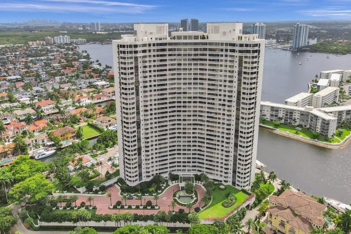 High-rise building featuring a curved architectural design, expansive glass balconies, a circular paved motor court with a central fountain, and lands