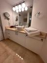 Vanity featuring a vessel sink, stone countertop, white cabinetry with metal hardware, large wall-mounted mirror, and multi-bulb overhead lighting