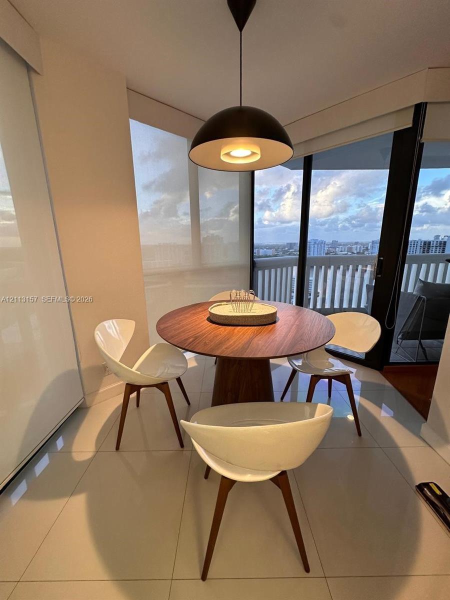 Polished tile flooring, matte black dome pendant lighting, floor-to-ceiling glass wall, and balcony access