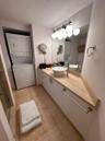 Custom vanity featuring a wood-tone countertop, vessel sink with a tall faucet, large wall-mounted mirror, multi-globe light fixture, and integrated l