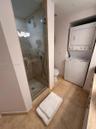 Walk-in shower with a glass door, stone-finish wall tiling, integrated stacked laundry unit, and stone-finish floor tiling