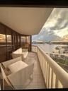 Covered balcony featuring expansive glass paneling, tile flooring, and a white vertical railing, overlooking an expansive water landscape and urban sk