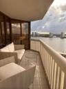 Covered balcony featuring tile flooring, metal railings, and floor-to-ceiling tinted glass panels overlooking the water and urban skyline