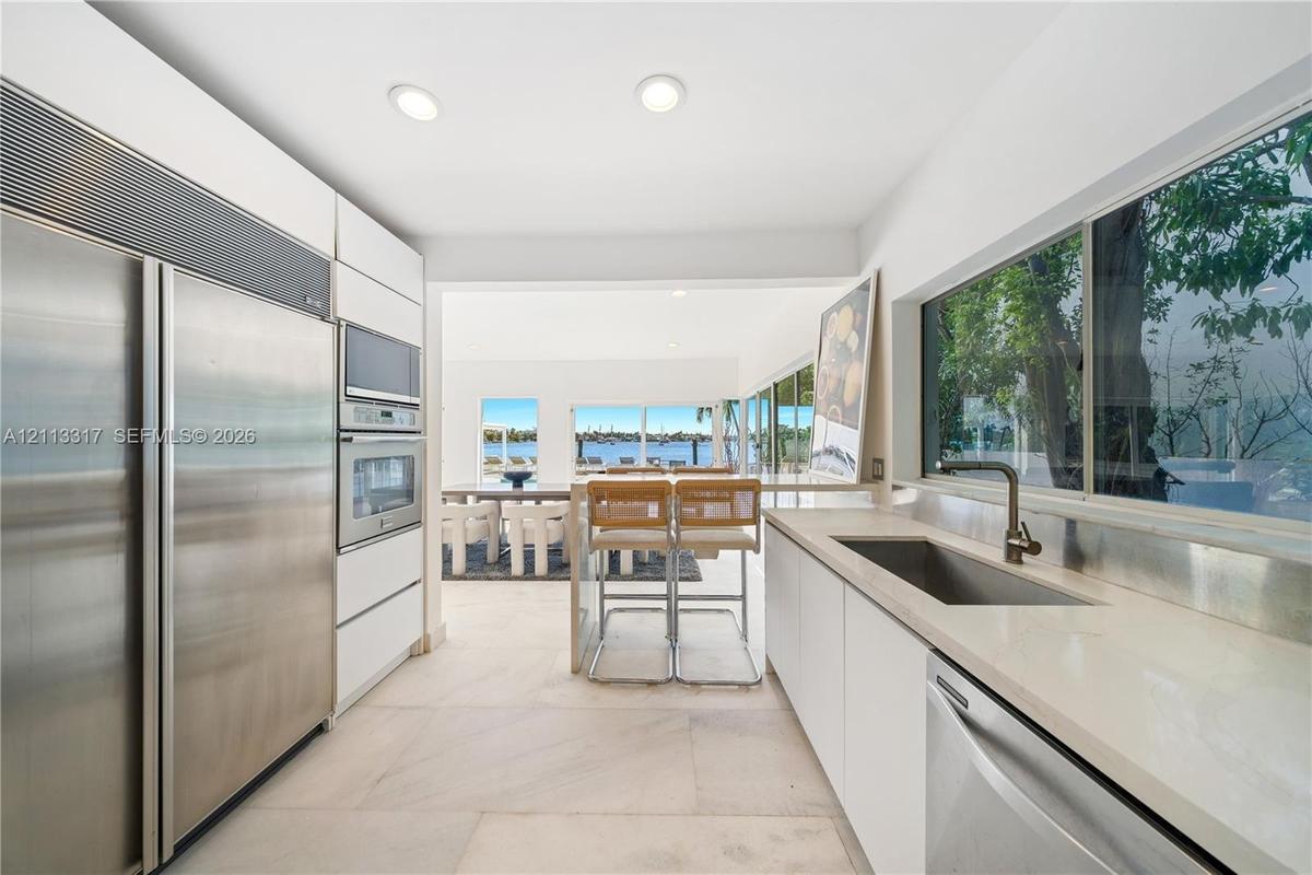 Kitchen featuring custom flat-panel cabinetry, professional-grade stainless steel appliances, stone countertops, integrated sink, and large-format til