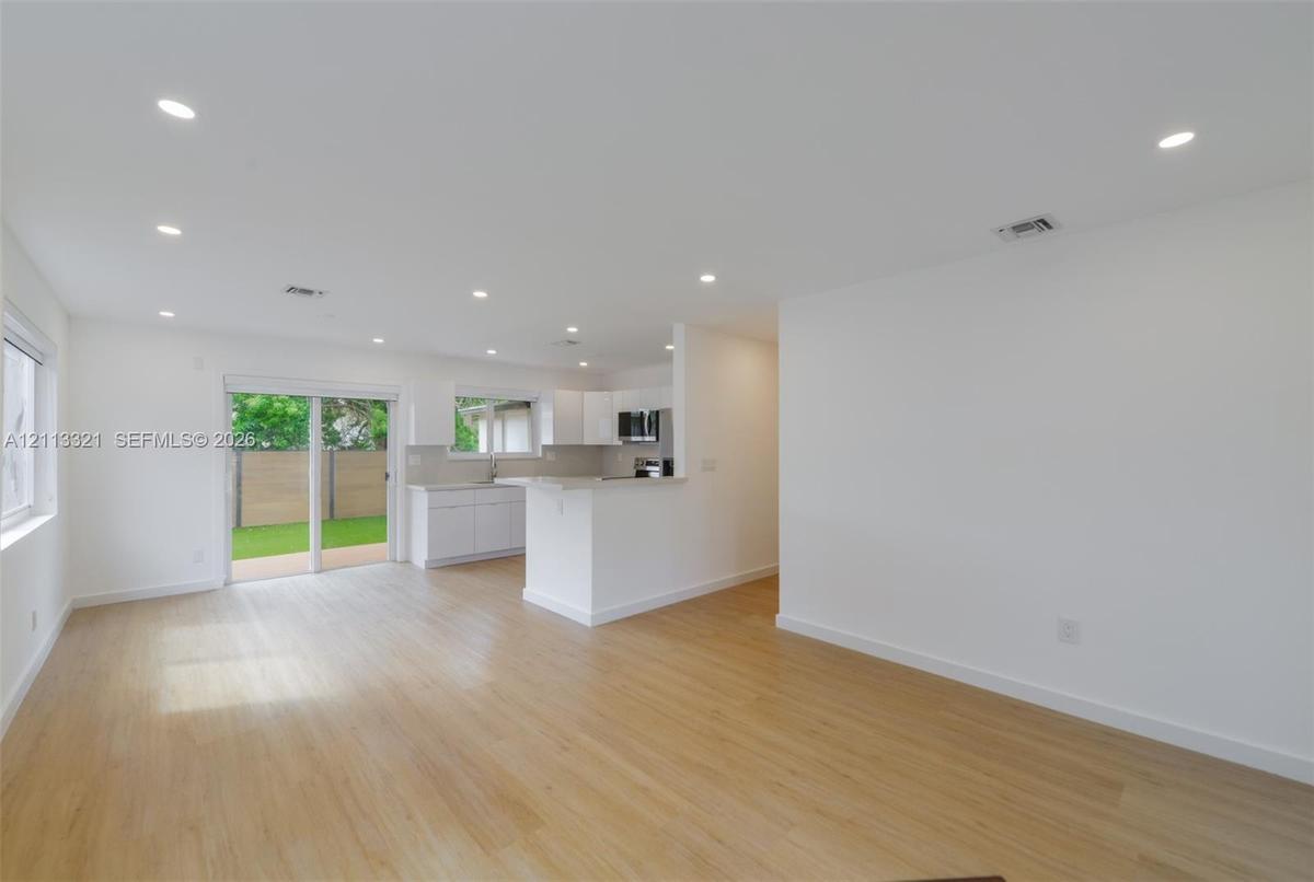 Open interior featuring wood-finish flooring, recessed lighting, white cabinetry, a peninsula counter, and sliding glass doors