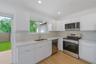Kitchen featuring high-gloss white cabinetry, stainless steel appliances, light-toned stone countertops, recessed lighting, and wood-finish flooring