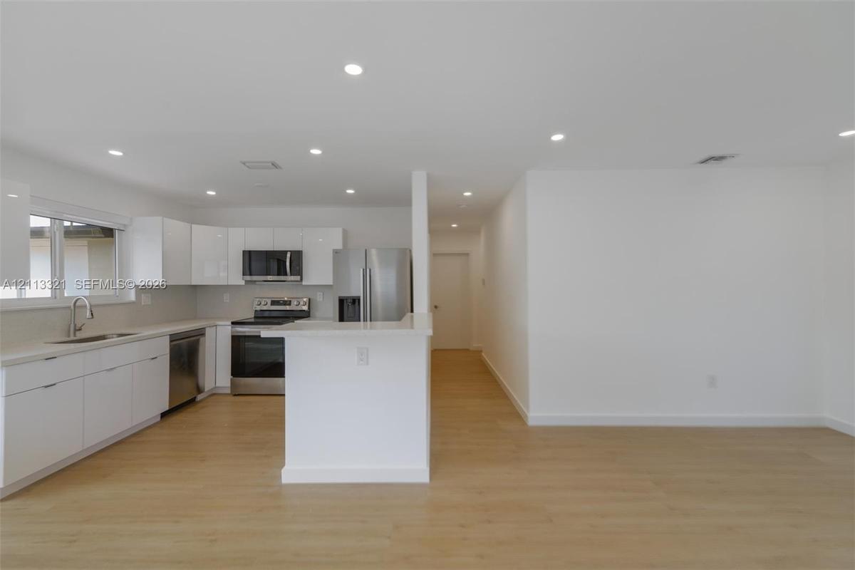 Kitchen featuring white high-gloss cabinetry, stainless steel appliances, a peninsula with stone countertops, and wood-finish flooring illuminated by 