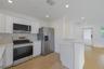 Modern kitchen featuring white flat-panel cabinetry, light-toned countertops, stainless steel appliances, wood-finish flooring, and recessed lighting