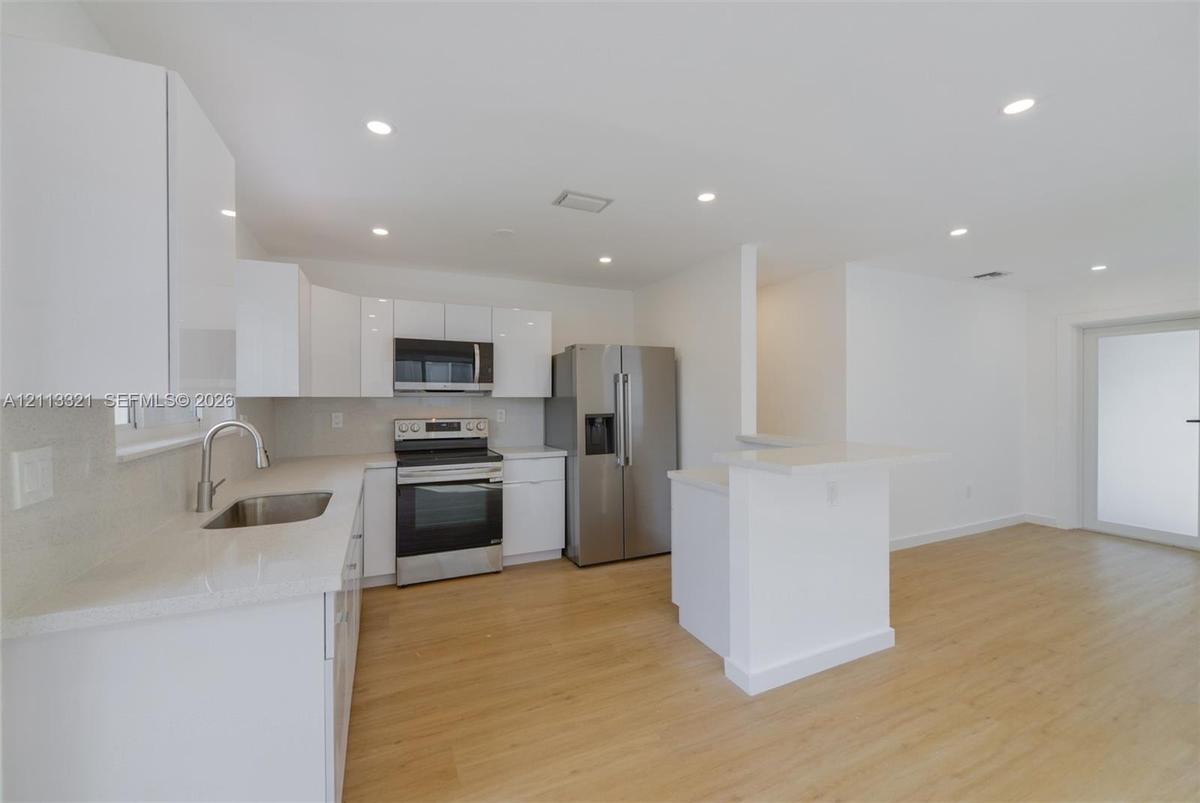 Kitchen featuring high-gloss white cabinetry, stone-finish countertops, stainless steel appliances, recessed lighting, and wood-finish flooring