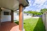 Covered patio with wood-finish decking and vertical slat support columns, featuring synthetic turf, concrete paver accents, and perimeter privacy fenc