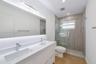 Dual-sink vanity with white stone-finish countertop, under-mount sinks, chrome faucets, full-width mirror with integrated lighting, and glass-enclosed