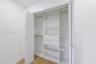 Custom reach-in closet featuring white built-in shelving, dual integrated drawers, hanging rods, and bi-fold doors, accented by wood-finish flooring