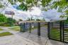 Black metal horizontal-slat gate with a concrete driveway and mature trees