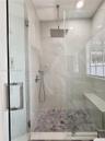 Walk-in shower featuring a frameless glass enclosure, ceiling-mounted rainfall showerhead, handheld sprayer, built-in bench, and grey hexagonal floor 