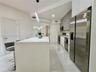 Kitchen featuring a waterfall-edge island with stone-finish countertop, high-gloss flat-panel cabinetry, stainless steel appliances, and large-format 