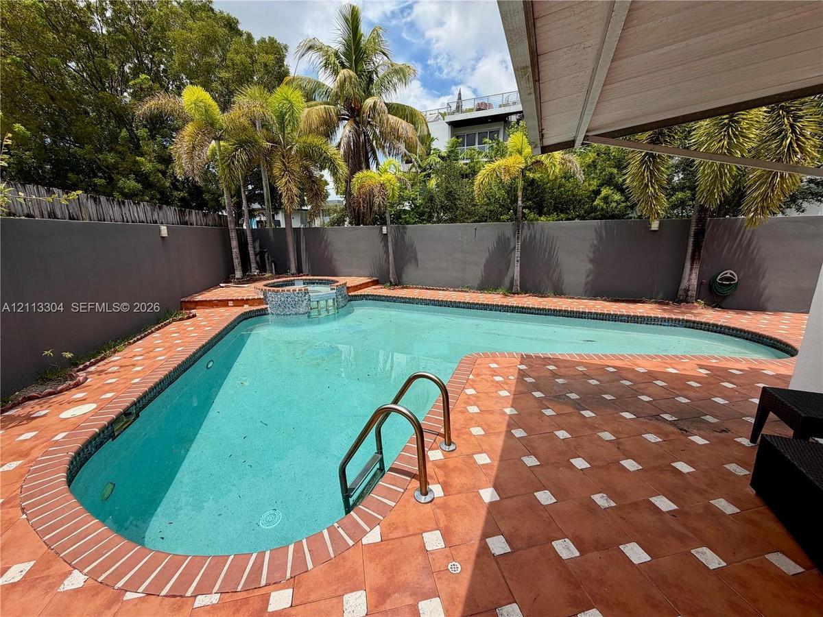 Backyard featuring an inground pool with tile coping, an attached spa, terra cotta paver hardscaping, perimeter masonry walls, and mature palm trees