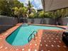 Backyard featuring an inground pool with tile coping, an attached spa, terra cotta paver hardscaping, perimeter masonry walls, and mature palm trees