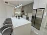 Kitchen featuring a waterfall-edge island with stone-finish countertop, high-gloss cabinetry, stainless steel appliances, and linear pendant lighting