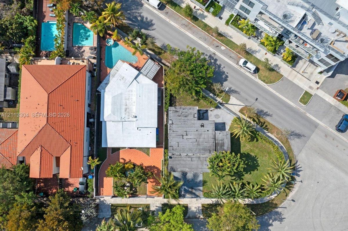 Aerial view of property featuring a swimming pool, paved patio, and mature palm trees