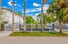 Exterior street-level view featuring a decorative metal perimeter fence with masonry pillars, manicured grass area, mature palm trees, and exterior po