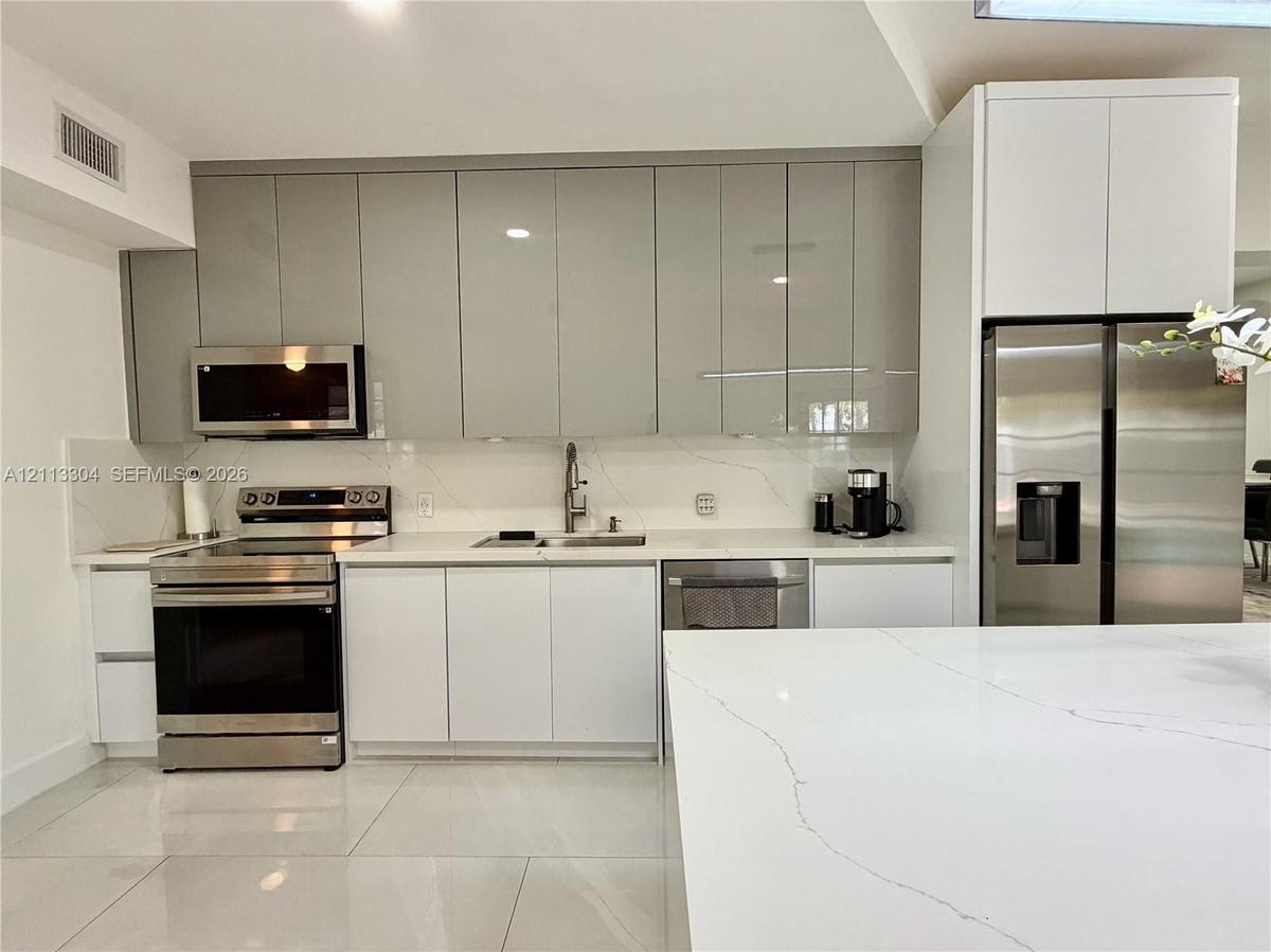 Kitchen featuring high-gloss cabinetry, stone-finish countertops with matching backsplash, stainless steel appliances, and large-format tile flooring