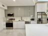 Kitchen featuring high-gloss cabinetry, stone-finish countertops with matching backsplash, stainless steel appliances, and large-format tile flooring