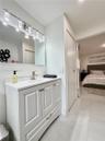 White vanity with shaker-style cabinetry, solid-surface countertop with an integrated sink, polished metal hardware, and a multi-bulb light fixture mo