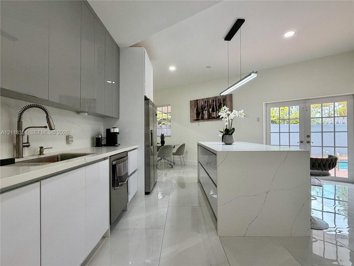 Modern kitchen featuring high-gloss cabinetry, a waterfall-edge stone island, polished tile flooring, and a linear pendant light fixture