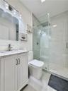 Bathroom featuring a white shaker-style vanity with a stone countertop, an integrated sink with a metallic faucet, a frameless glass-enclosed walk-in 