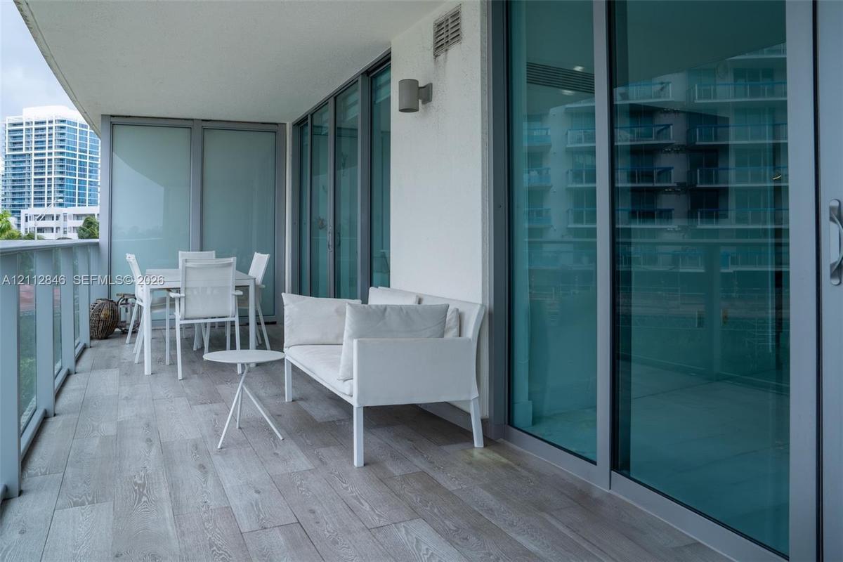 Covered balcony featuring wood-finish flooring, glass-panel railings, and floor-to-ceiling sliding glass doors