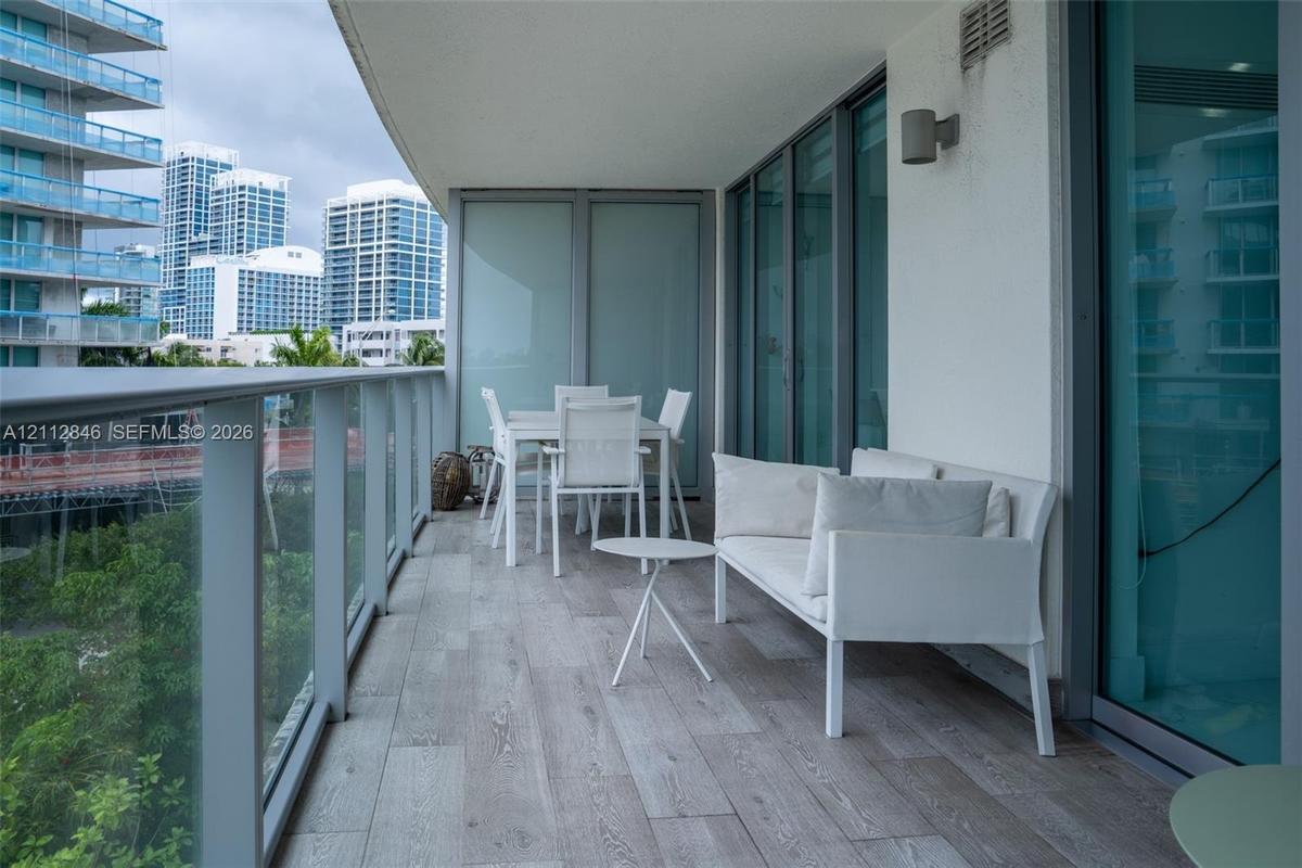 Covered balcony featuring wood-finish tile flooring, glass panel railings, and full-height sliding glass doors with brushed metal frames