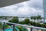 Covered balcony with a metal railing, overlooking an outdoor swimming pool, lush landscaping, and a waterfront setting