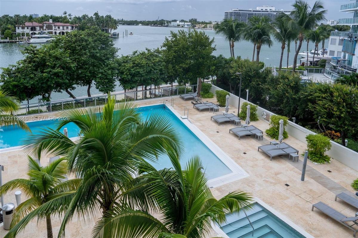 Waterfront pool and spa area featuring natural stone decking, integrated palm tree landscaping, and perimeter glass railing