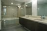 Dual-sink vanity with light-toned solid surface countertop and dark-finish cabinetry, complemented by a glass-enclosed wet room containing a soaking t
