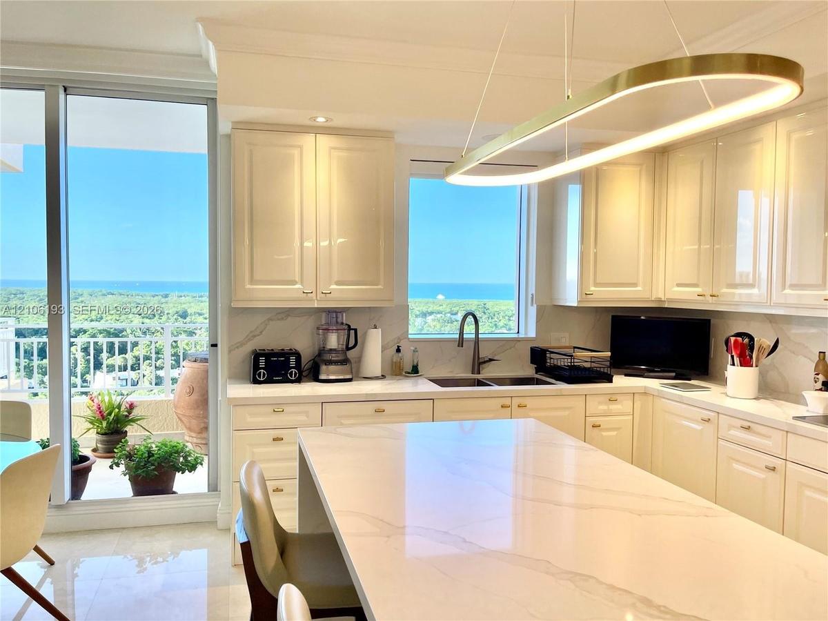 Kitchen featuring glossy cream cabinetry, a central island with a stone countertop, an integrated stainless steel dual-basin sink, and a circular LED 