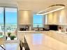 Kitchen featuring glossy cream cabinetry, a central island with a stone countertop, an integrated stainless steel dual-basin sink, and a circular LED 