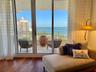 Floor-to-ceiling glass sliding doors, wood-finish flooring, and a stone-tiled balcony with metal railing