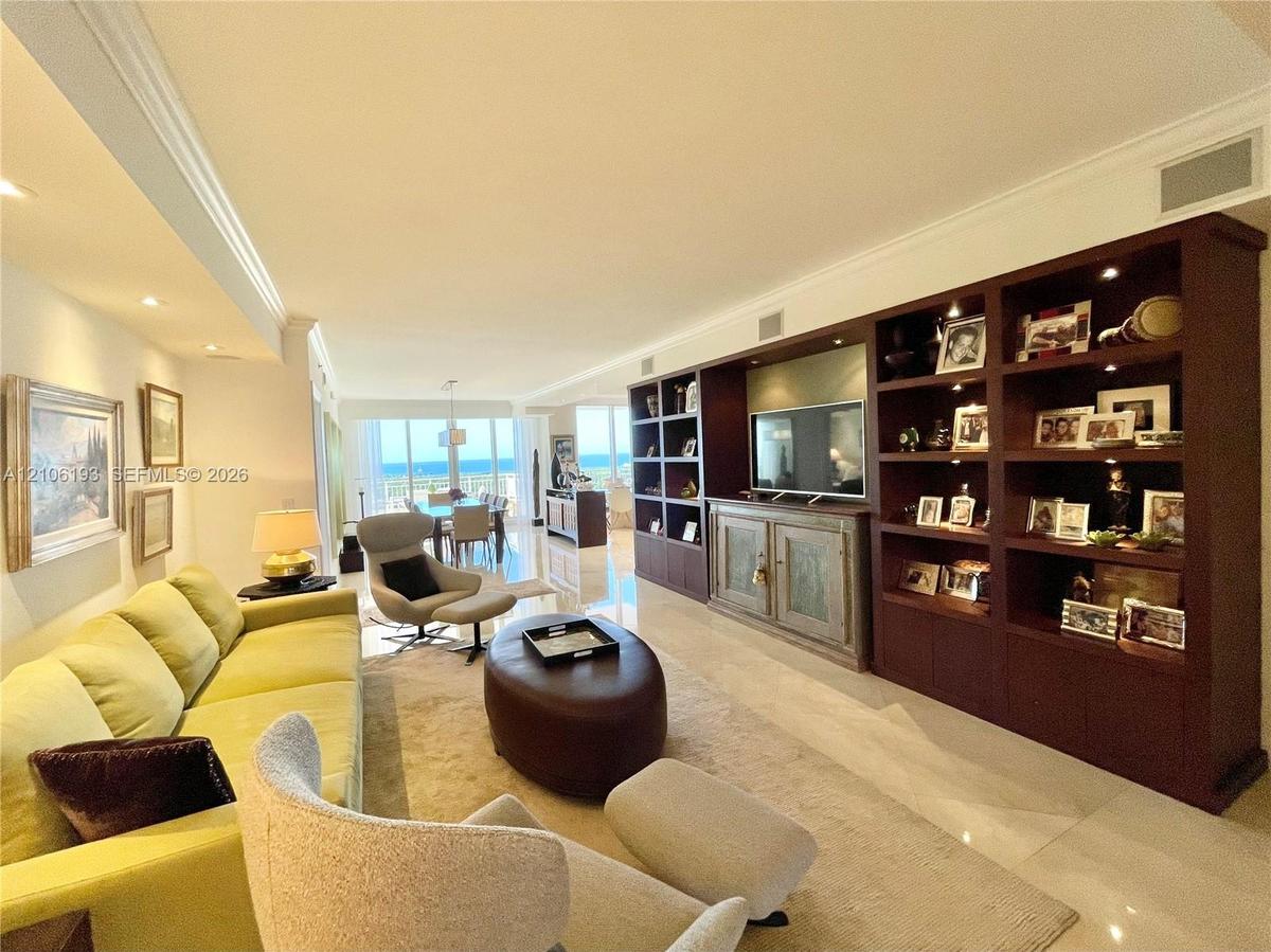 Large living area featuring polished stone flooring, extensive built-in floor-to-ceiling dark wood shelving, recessed lighting, and floor-to-ceiling w