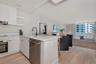 Kitchen featuring white flat-panel cabinetry, light-toned stone countertops, a stainless steel dishwasher, a matte black high-arch faucet, and light w