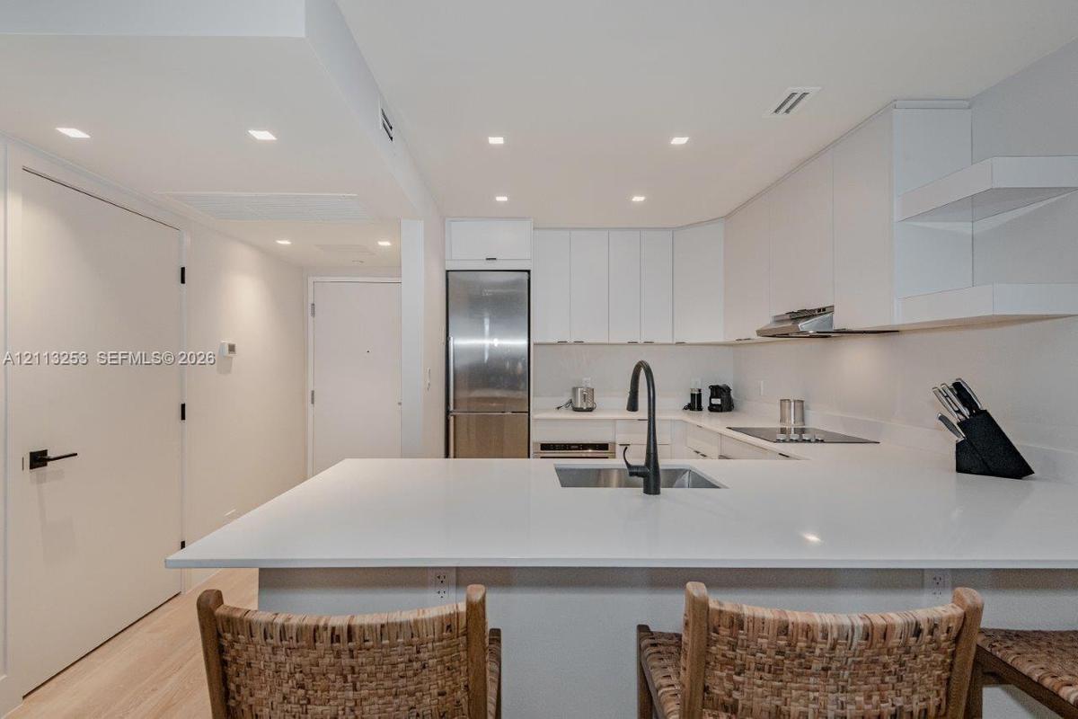 Kitchen featuring crisp white flat-panel cabinetry, solid-surface countertops, recessed ceiling lighting, stainless steel appliances, and a matte blac