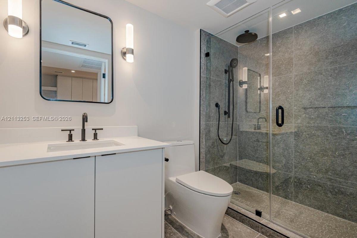 Bathroom featuring a vanity with quartz countertop, walk-in glass-enclosed shower with stone-tile surround, dual shower heads, and modern wall-mounted