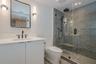 Bathroom featuring a vanity with quartz countertop, walk-in glass-enclosed shower with stone-tile surround, dual shower heads, and modern wall-mounted