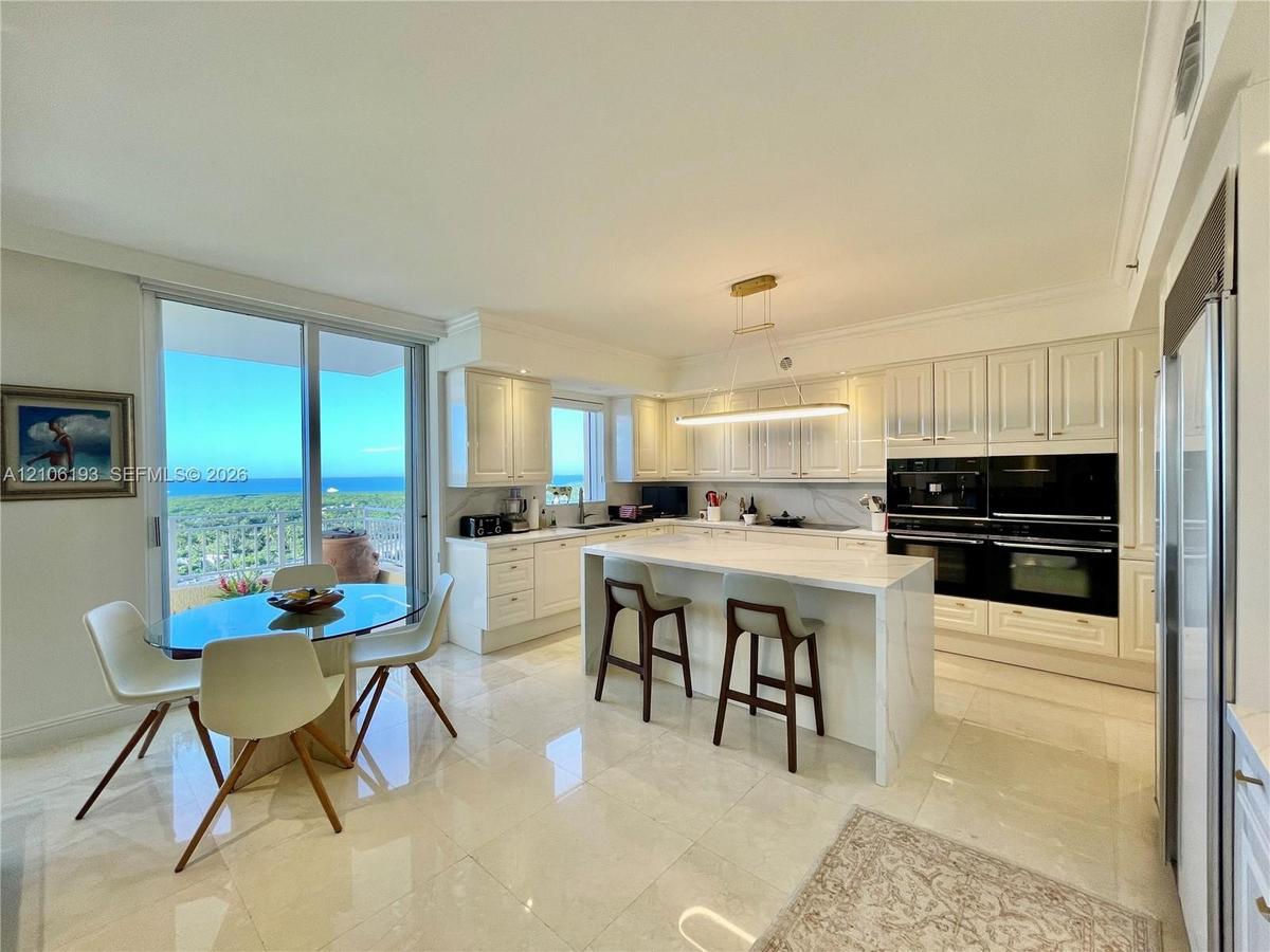 Kitchen featuring white cabinetry, an expansive center island with stone-finish countertops, built-in dual ovens, polished tile flooring, and sliding 